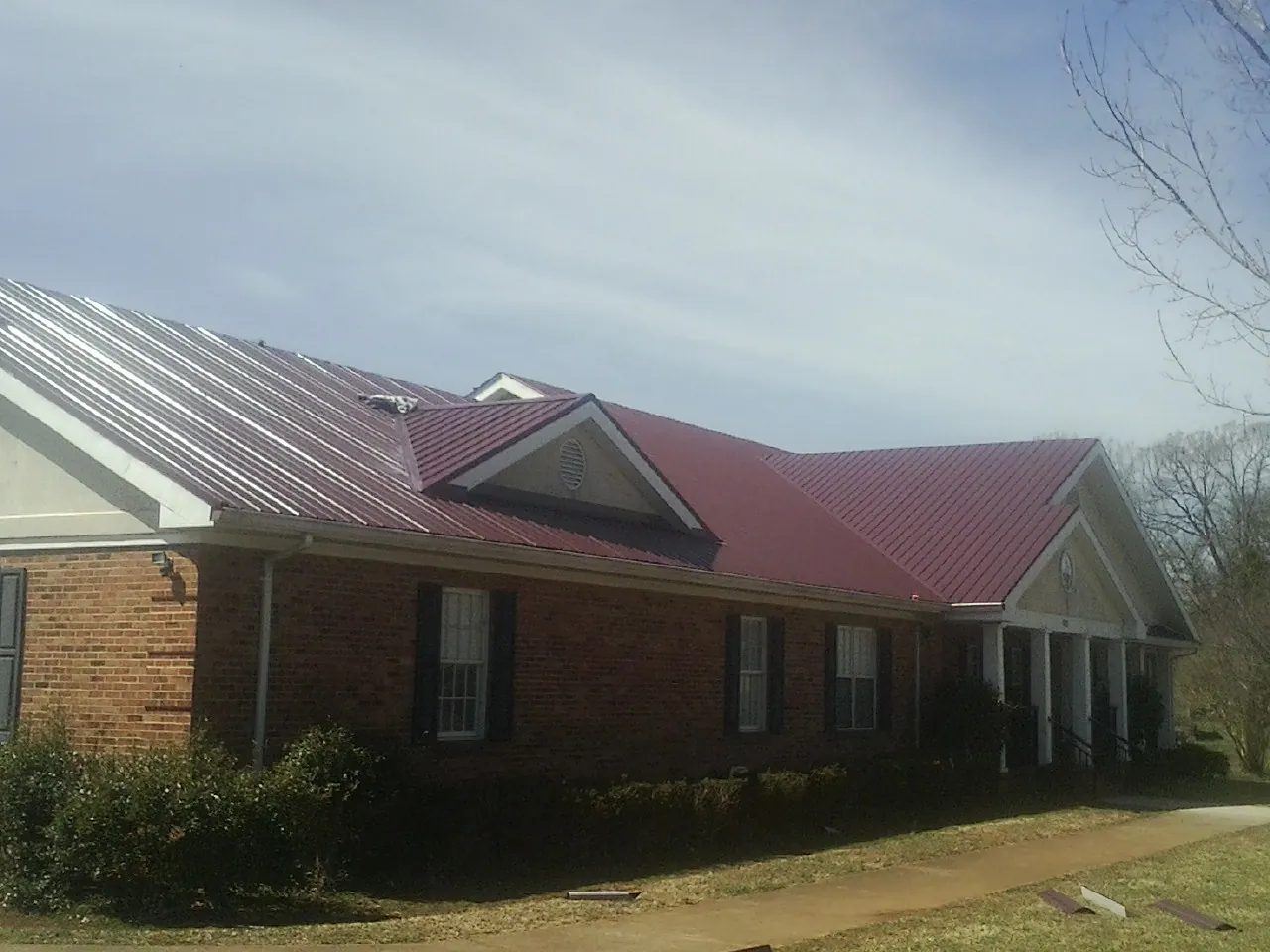 Red metal roof with gabled entries on a long brick building, from a Hail Damage Roof Repair job in Kechi