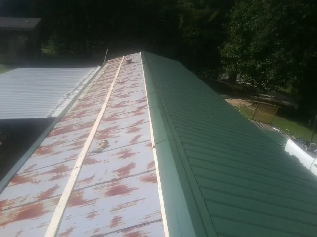 Old rusted panels beside newly installed green metal roofing — Wind Damage Roof Repair by Roofing Brothers in Kechi