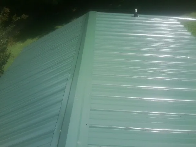 New green metal panels meeting at the ridge of a roof — Flat Roof Repair work by our crew in Kechi