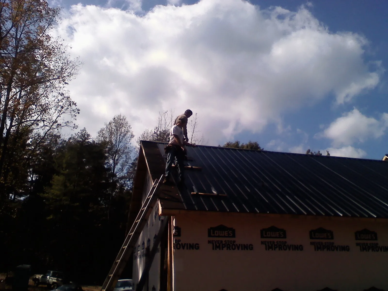 Roofer fastening dark metal panels high against a cloudy sky, from a Roof Inspection job in Kechi