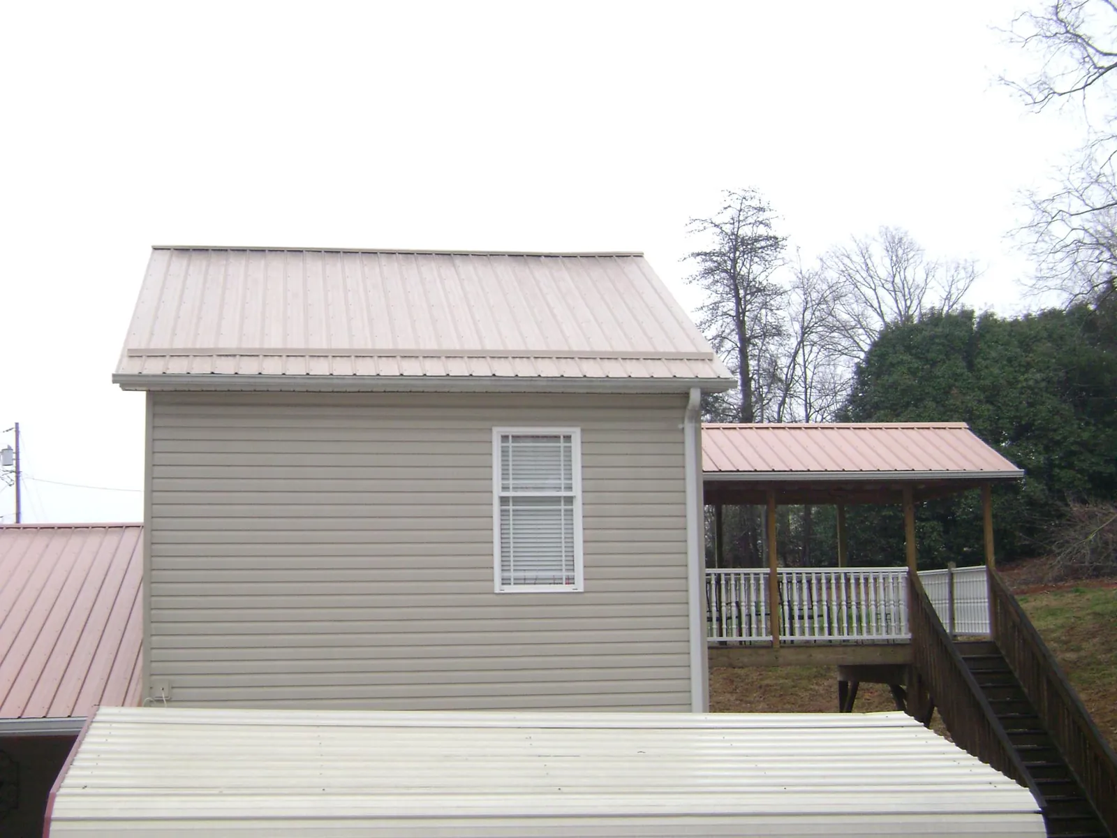 Tan metal roofs on a two story addition and attached porch, from a Roof Replacement job in Kechi